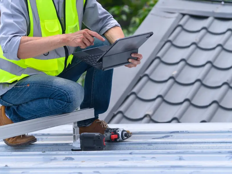 Roofing professional inspecting a tiled residential roof while using a tablet and power tools to assess roof condition and plan maintenance work in Sydney, NSW.
